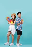 Young Asian couple in summer outfits with water guns in studio blue background. Songkran festival. photo
