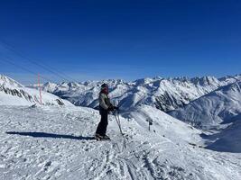 un persona en esquís en pie en un Nevado montaña foto