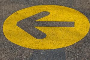 black arrow with a yellow circle pointing to the left is painted on a road photo