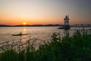 soltero kayakista remar en un ensenada a puesta de sol con un faro en el antecedentes foto