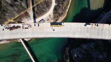 aérien drone vue de le construction de une haute béton pont plus de le rivière. Autoroute pont en dessous de construction. nombreuses haute grue Machines et ouvriers sur le construction placer. video