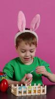 joven adorable niños colorante Pascua de Resurrección huevos con acuarela pintar, creando encantador diseños a celebrar primavera día festivo. alegre hermano y hermana pintura festivo decoraciones en estudio. cámara b. video