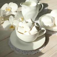 Spring breakfast with marshmallow, coffee and milk. Flatlay with food and flower in white color photo