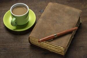 antique leather-bound journal with decked edge handmade paper pages and a stylish pen on a rustic wooden table with coffee, journaling concept photo