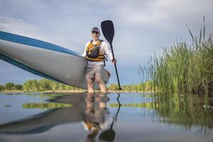 senior male paddler is launching a stand up paddleboard on a calm lake in spring, frog perspective from an action camera at water level photo
