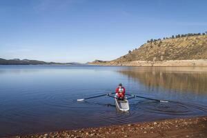 Senior male rower is rowing a coastal rowing shell - Carter Lake in fall or winter scenery in northern Colorado. photo