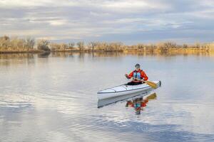 senior male paddler is paddling a decked expedition canoe on a calm lake in northern Colorado, winter scenery without snow photo