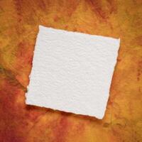 small square sheet of blank white Khadi paper against colorful marbled paper photo