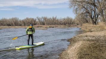 male paddler in paddling upstream on an inflatable stand up paddleboard - South Platte River in Colorado in early spring scenery photo