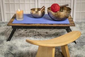 large Tibetan singing bowl with a mallet, roller and wax candle on a low table, and kneeling bench, sound healing and meditation concept photo