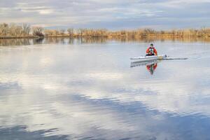 senior male paddler is paddling a decked expedition canoe on a calm lake in northern Colorado, winter scenery without snow photo