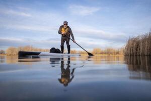 senior paddler on his paddleboard on lake in winter or early spring in Colorado, frog perspective, partially submerged action camera photo