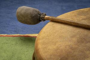 handmade, native American style, shaman frame drum covered by goat skin with a beater against colorful abstract paper landscape photo