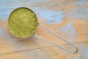 measuring scoop of organic matcha green tea powder against grunge wood photo