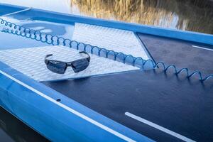 Gafas de sol y un enroscado la seguridad Correa en un mojado cubierta de estar arriba paddleboard foto