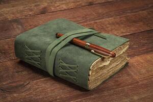 retro leather-bound journal with decked edge handmade paper pages with a stylish pen on a rustic barn wood table, journaling concept photo