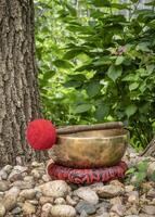 handmade tibetan singing bowl with a mallet and cushion in outdoor setting, sound therapy for healing, relaxation and meditation photo