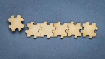 row of wooden jigsaw puzzle on blue background, completing a task or solving a problem concept photo