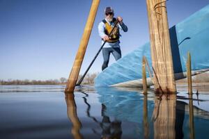 cañas en un calma lago en primavera con un fuera de atención estar arriba palista, rana perspectiva desde un acción cámara a agua nivel foto