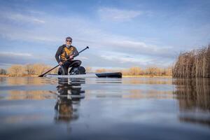 senior paddler and his paddleboard on lake in winter or early spring in Colorado, frog perspective, partially submerged action camera photo