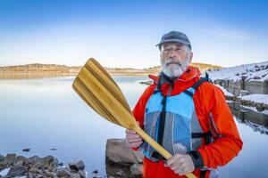 senior canoe paddler wearing life jacket on a shore of Carter Lake in northern Colorado in winter scenery photo