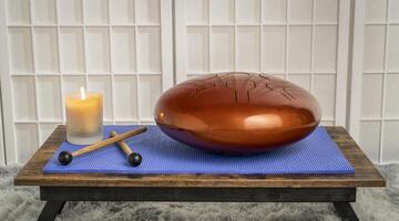 steel tongue drum with mallets and candle on a low table, sound healing and meditation concept photo