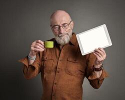 sonriente mayor hombre es Bebiendo café y demostración un blanco digital tableta foto