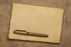 sheets of blank handmade paper with rough edges and a stylish pen against textured bark paper photo