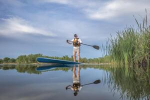 senior male paddler is paddling  a stand up paddleboard on a calm lake in spring, frog perspective from an action camera at water level photo