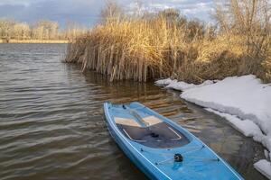 touring stand up paddleboard with a safety leash on a shore of lake in northern Colorado, winter or early spring scenery with some snow photo