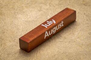 July and August text on wooden block against handmade bark paper in earth tones, calendar concept photo