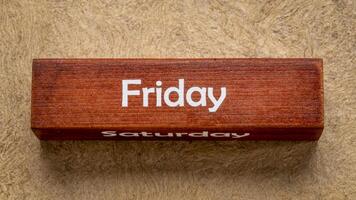 Friday and Saturday text on wooden block against handmade bark paper in earth tones, calendar concept photo