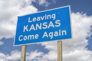 Leaving Kansas, come again - roadside sign at highway against cloudy sky photo