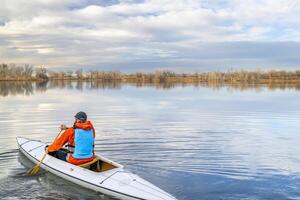 senior male paddler is paddling a decked expedition canoe on a calm lake in northern Colorado, winter scenery without snow photo