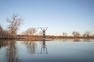 happy senior paddler is paddling stand up paddleboard on calm at sunset in early spring in Fort Collins, Colorado lake, frog perspective, partially submerged action camera photo