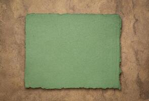 green and brown abstract - a sheet of blank Indian handmade rag paper against textured bark paper, copy space photo