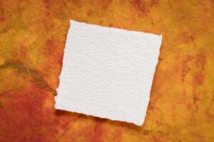 small square sheet of blank white Khadi paper against colorful marbled paper photo