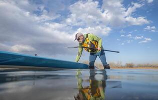 senior paddler and his paddleboard on lake in winter or early spring in Colorado, frog perspective, partially submerged action camera photo