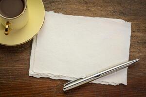 small sheet of blank white Khadi rag paper on rustic wooden table with coffee photo