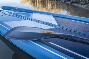 wet paddle and a coiled safety leash on a deck of stand up paddleboard photo