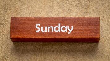 Sunday text on wooden block against handmade bark paper in earth tones, calendar concept photo