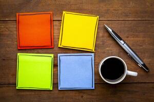 set of colorful, blank reminder notes on a grunge wooden table with a cup of espresso coffee and pen photo