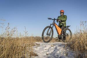 senior cyclist with a mountain bike on a trail covered by snow photo