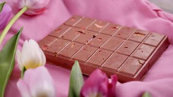 un bar de rosado rubí chocolate con sublimado liofilizado fresas y Almendras y primavera tulipán flores . un postre establecido en bayas y nueces para internacional De las mujeres día, marzo 8, de la madre día foto