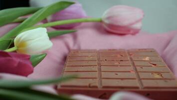 A bar of pink ruby chocolate with sublimated freeze-dried strawberries and almonds and spring tulip flowers . A dessert based on berries and nuts for International Women's Day, March 8, mother's day photo