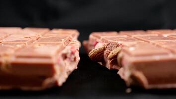 A bar of pink ruby chocolate with freeze-dried strawberries and almonds close-up, isolated black background. A healthy dessert based on berries and nuts photo