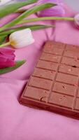 A bar of pink ruby chocolate with sublimated freeze-dried strawberries and almonds and spring tulip flowers . A dessert based on berries and nuts for International Women's Day, March 8, mother's day photo