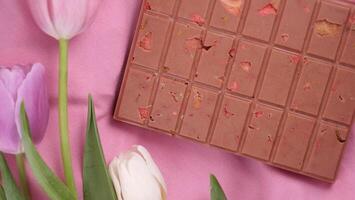 A bar of pink ruby chocolate with sublimated freeze-dried strawberries and almonds and spring tulip flowers . A dessert based on berries and nuts for International Women's Day, March 8, mother's day photo