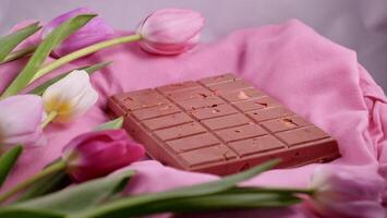 A bar of pink ruby chocolate with sublimated freeze-dried strawberries and almonds and spring tulip flowers . A dessert based on berries and nuts for International Women's Day, March 8, mother's day photo