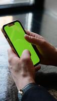 Close-up smartphone with green screen in men's hands. A businessman scrolls the phone with chroma key in the office. Vertical photo